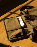 A brown heavyweight cotton Utility Tote Bundle - Set of 3 with an open exterior pocket holding a notebook and glasses.