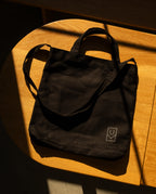 Sturdy black Ugmonk Utility Tote (Black) canvas bag with a small logo printed on the lower corner, resting on a wooden surface.