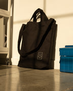 A durable heavyweight cotton canvas Utility Tote Bundle - Set of 3 with a small logo leaning against a white wall next to a blue plastic box.
