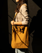 A person carrying a mustard-colored heavyweight cotton Utility Tote Bundle - Set of 3 with a small logo on the front.
