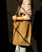 A person wearing a durable heavyweight cotton canvas Utility Tote Bundle - Set of 3 with a small white logo on the bottom corner.