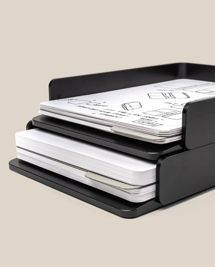 A black Analog Capture Kit - 2 Large (Black Aluminum) holds two notebook stacks and a sleek card tray with dot grid cards—perfect for organizing sketches and notes. One stack is on the top shelf; the other is below, set against a plain beige background.