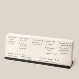 The Analog Weekly Planning Kit (Black Aluminum) is a minimalist desk calendar on a sleek stand, perfect for organizing handwritten meal and event plans like shrimp risotto dinners, takeout nights, and brunch with friends.