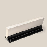 A closed book stands upright in a sleek, black Analog Weekly Planning Kit (Black Aluminum) against a light beige background. The stand supports the bottom edge, ideal for displaying Weekly Cards or organizing your planning kit essentials.