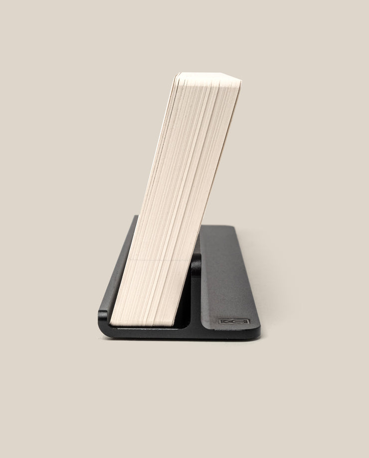 The Complete Analog Collection (Black Aluminum) holds a thick stack of paper or cards upright in a sleek black organizer against a plain beige background.