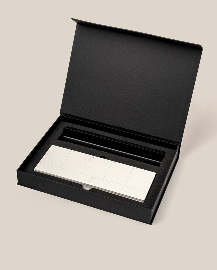 The Analog Weekly Planning Kit (Black Aluminum) features a sleek silver aluminum card stand with multiple rectangular buttons, nestled in a black foam insert inside an open black box set against a beige background.