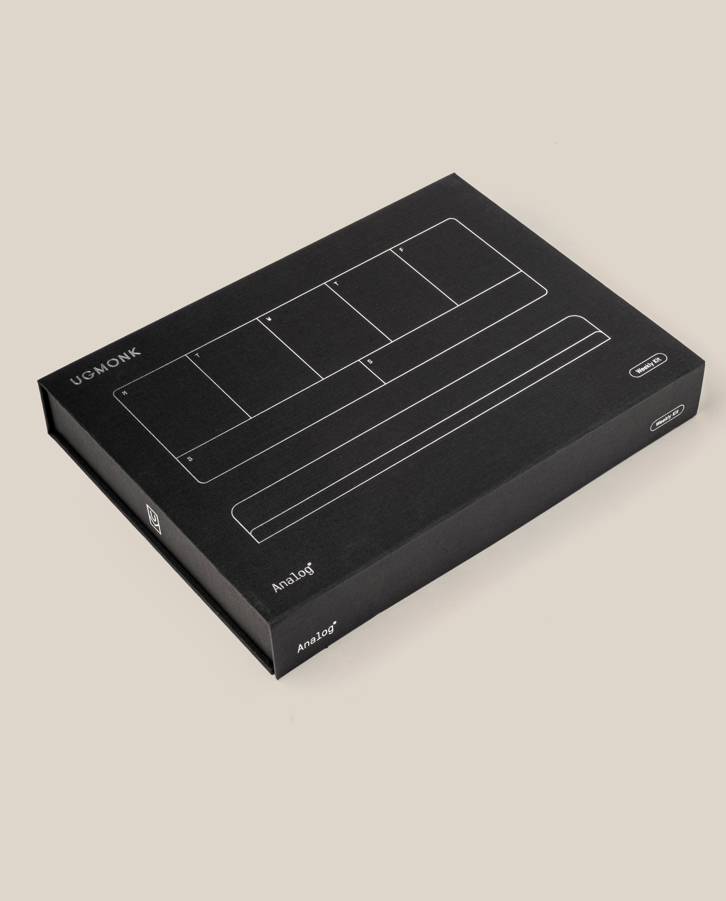A black rectangular box with white line illustrations and "UGMONK" and "Analog" on the lid, featuring the Analog Weekly Planning Kit (Silver Aluminum), is placed on a plain beige background.