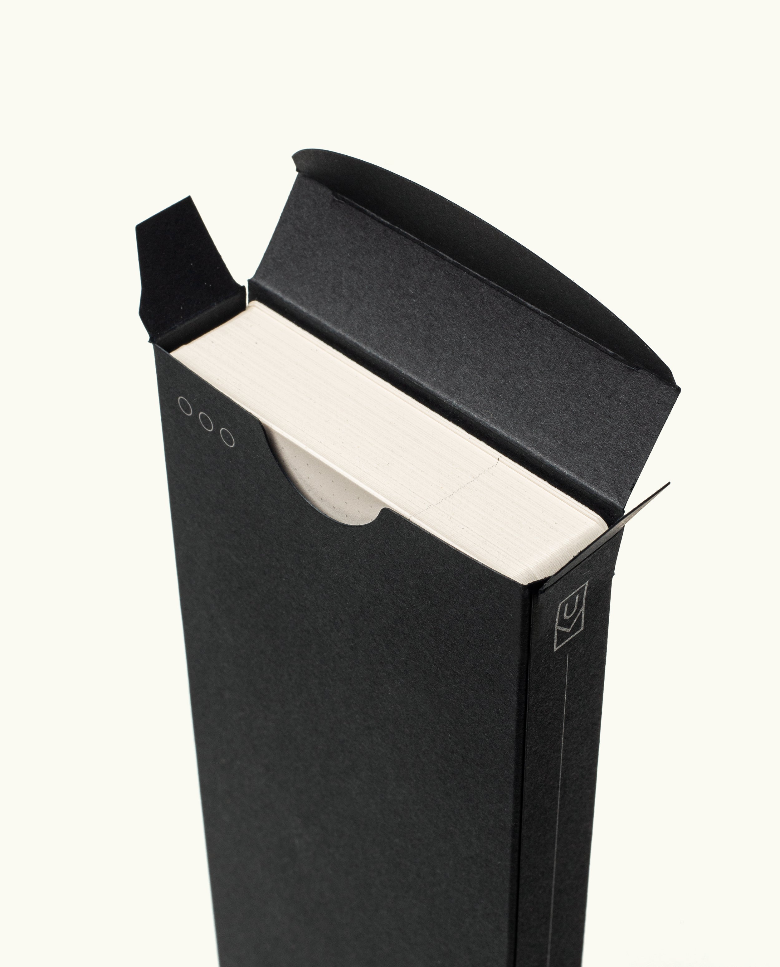 A minimal black cardboard box with a circular cutout partially reveals the edges of Analog Weekly Cards, featuring simple line accents for easy access and a clean design.