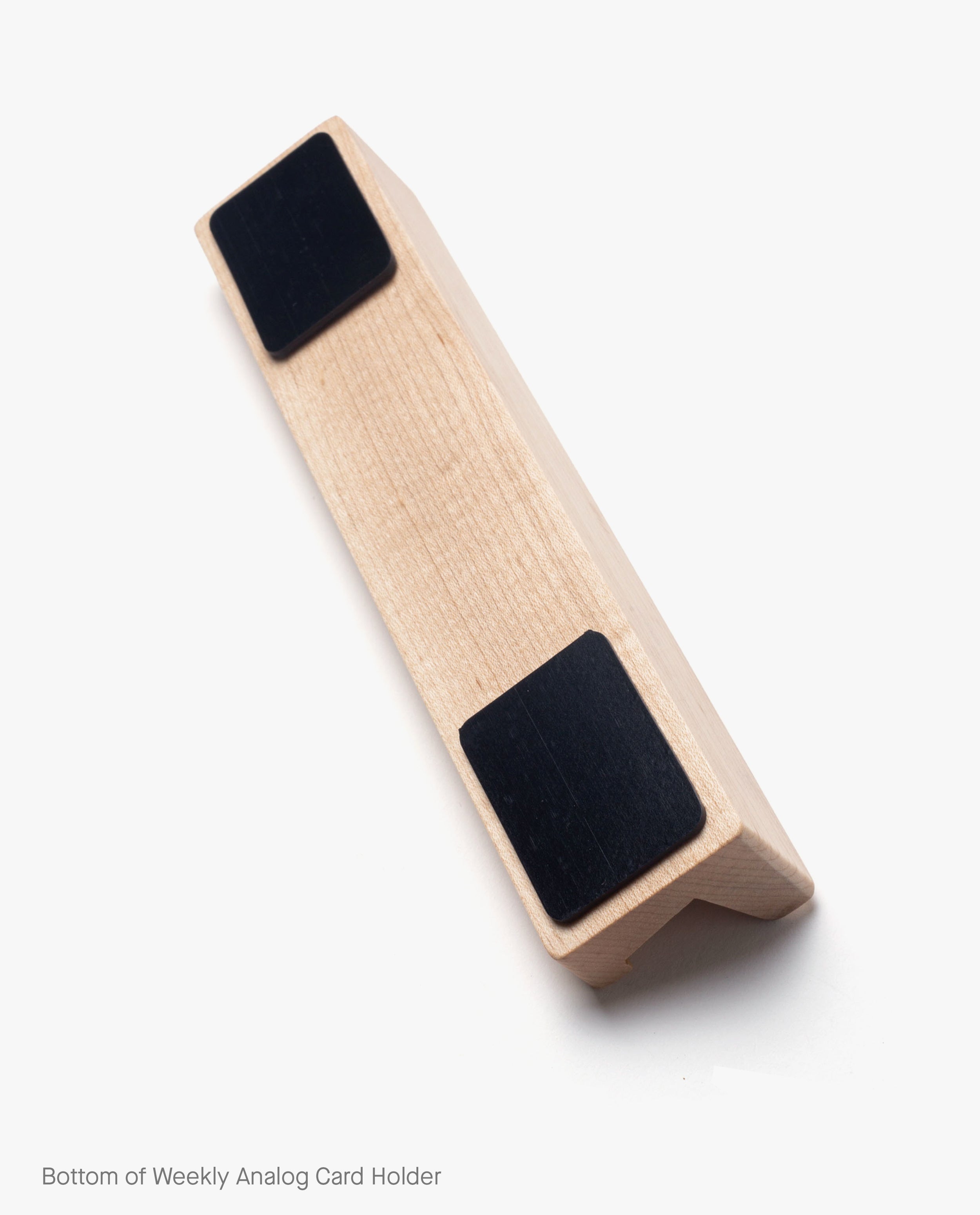 A wooden block with two black rectangular pads on the bottom, angled on a white background. Text on the image reads, Bottom of Magnet Kit (Pen Tray and Analog Weekly). Subtle magnets are embedded to securely attach accessories.