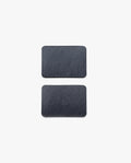 Two rectangular, dark gray slate pieces with rounded corners from the Magnet Kit (Pen Tray and Analog Weekly) are placed vertically on a plain white background, spaced evenly apart—these streamlined accessories are designed to complement your Gather Monitor Stand or Pen Tray. Cleverly integrated magnets help keep these sleek pieces securely in place on your workspace.
