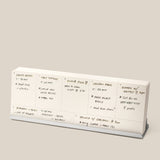 The Analog Weekly Planning Kit (Silver Aluminum) is shown on a stand with handwritten daily notes for meals, prep times, ingredients, and a dinner event with friends. The background is plain beige.