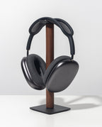 Sleek, over-ear black headphones with a mesh headband rest on the Gather Headphone Stand (1x1 - Black/Walnut), crafted from solid wood and powder-coated steel, displayed against a plain white background.