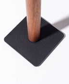 The Gather Headphone Stand (1x1 - Black/Walnut) features a solid walnut cylindrical pole set into a flat, black powder-coated steel square base, creating a minimalist look against a bright white background.