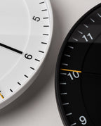 Close-up of two modern wall clocks—a white easy-to-read clock showing numbers 4 to 6 and a black Braun Wall Clock, both with minimalist designs and styled for contemporary spaces.
