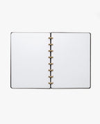The Discbound Heirloom Journal Bundle (Black Leather - Standard 6" x 8.5" + 3 Refills) is open to blank white pages, showcasing its gold-colored ring binding, viewed from above on a white background.