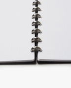 A close-up, low-angle view of the Discbound Heirloom Journal Bundle (Black Leather - Standard 6" x 8.5" + 3 Refills), featuring dotted pages and central metal disc binding connecting both sides of this sleek refillable notebook.