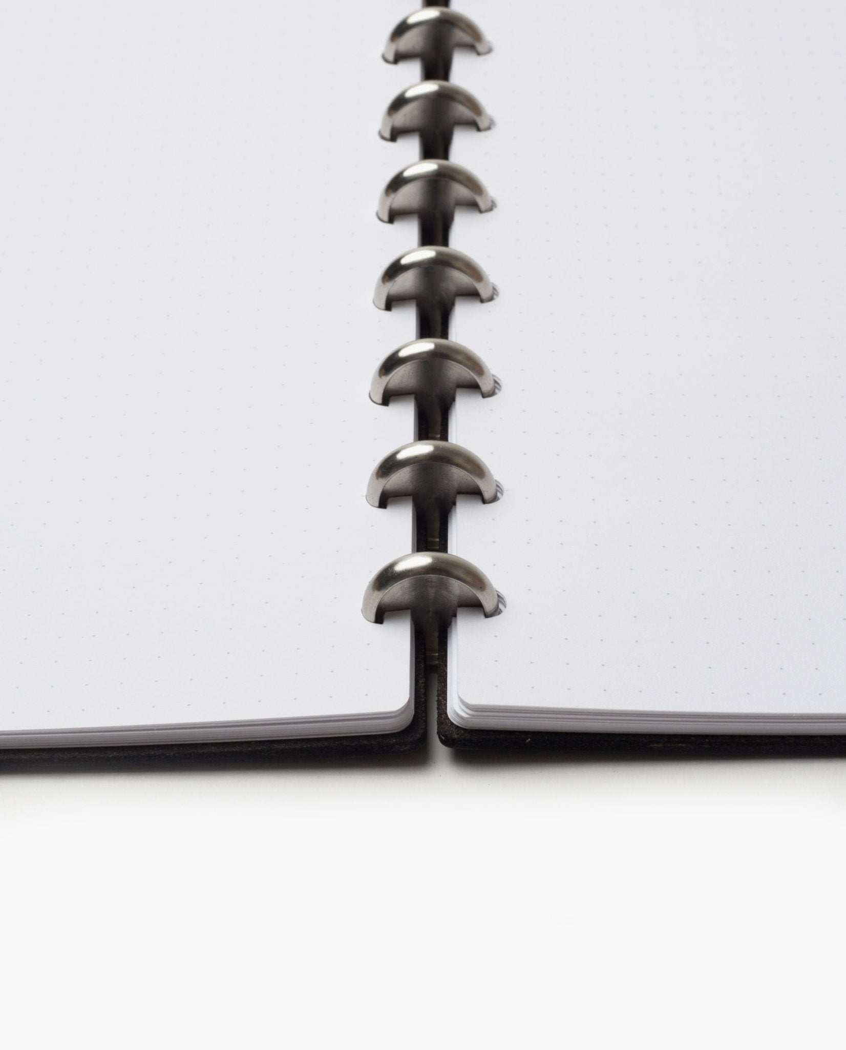A close-up, low-angle view of the Discbound Heirloom Journal Bundle (Black Leather - Standard 6" x 8.5" + 3 Refills), featuring dotted pages and central metal disc binding connecting both sides of this sleek refillable notebook.