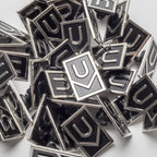 A collection of Ugmonk Enamel Pins with a geometric U-shaped design in black and silver, scattered and overlapping on a white surface.