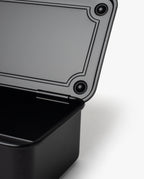 A close-up of an open Toyo Steel Stackable Storage Box T-190 (Black) with its lid partially raised, revealing the interior and textured lid edge against a white background, highlighting its functional design.